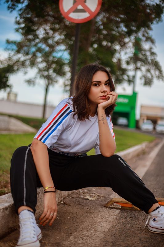 Light-skinned person wearing athletic clothes, sitting on a sidewalk curb and scowling